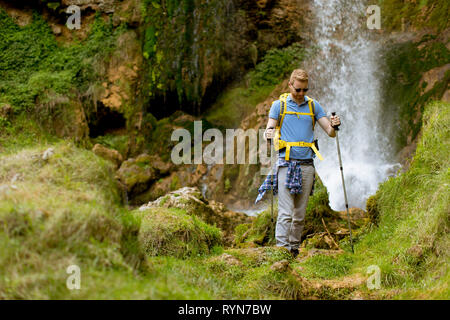 Bel giovane escursionista fermato accanto a una cascata di montagna di prendere un periodo di riposo Foto Stock