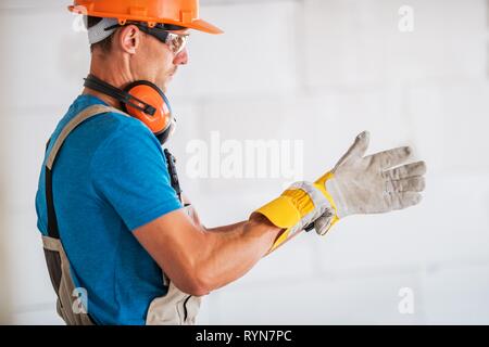 Lavoratore caucasici in elmetto e occhiali di sicurezza indossando guanti di sicurezza e preparazione per il lavoro. Industria di costruzione del tema. Foto Stock