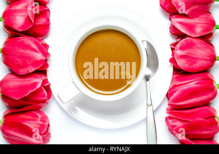 White tazza da caffè sorge su una piastra bianca con sfondo bianco vicino a multi-colore di tulipani. Primo piano Foto Stock