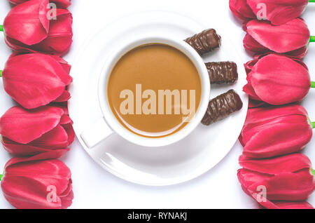 White tazza da caffè sorge su una piastra bianca con sfondo bianco vicino a multi-colore di tulipani. Primo piano Foto Stock