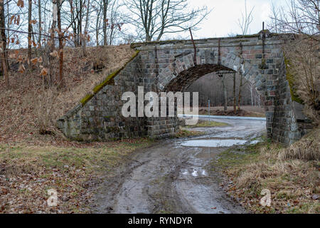 Stone viadotto sopra la vecchia linea ferroviaria. Una strada sterrata che conduce al di sotto di un vecchio ponte ferroviario. Stagione della primavera. Foto Stock