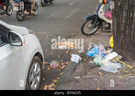 La città di Ho Chi Minh, Vietnam - Gennaio 8, 2019: un mucchio di immondizia sul marciapiede sotto un albero al centro della città con il traffico della strada visto. Foto Stock