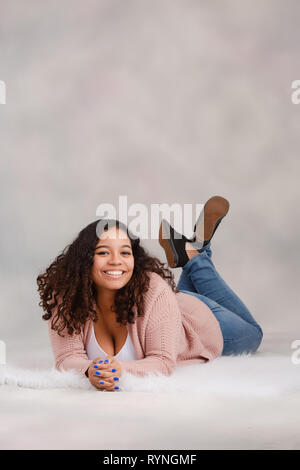 Attraente biracial high school senior recante sul pavimento e sorridente in posa per ritratti da studio Foto Stock