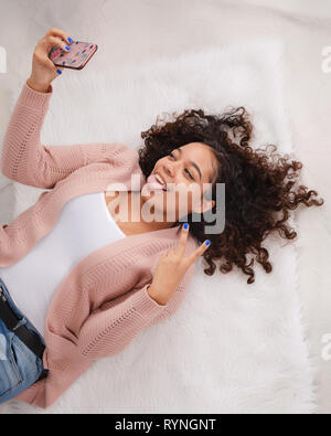 Attraente biracial high school senior recante sul pavimento e sorridente in posa per selfie per andare sui social media Foto Stock