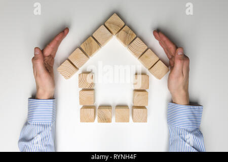 Casa di blocchi di legno. Giocattolo di legno casa protetta da donna con le mani in mano. Il concetto di protezione home Foto Stock