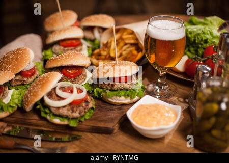 Close up di hamburger freschi con un bicchiere di birra su vintage tavolo in legno. Deliziosi piatti a base di carne. Gustosi sottaceti. Pane fresco. Ottima birra. Foto Stock