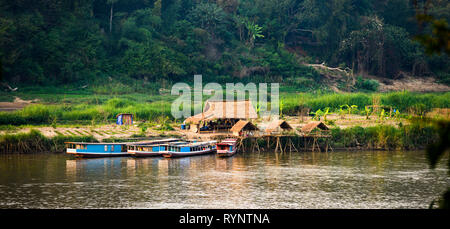 Bella tradizionali capanne con verdi campi in background e barche di legno ancorato sul fiume Mekong. Foto Stock