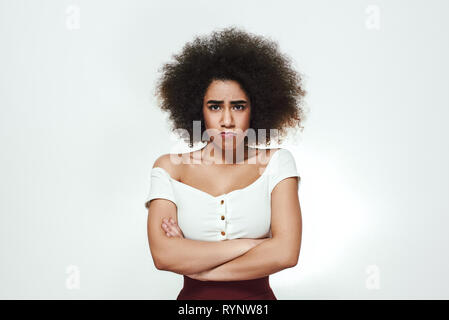 Meglio non toccare me! Annoiati giovani afro American donna tenere le braccia incrociate e rendendo il volto triste e stando in piedi contro uno sfondo grigio. Turbare la donna. Concetto di tristezza Foto Stock