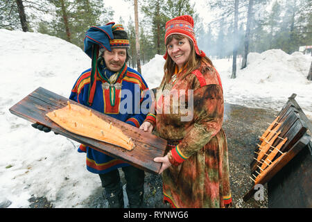 Saariselka, Finlandia - 24 aprile 2013: Locale saami giovane azienda tavola di legno con un salmone affumicato filetto preparato su open air fire in Saariselka, Fin Foto Stock