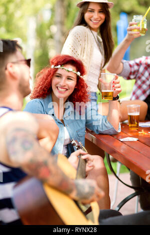 Giovani felice parentesi dai capelli rossi ragazza brinda con hipster ragazzo con la chitarra al di fuori Foto Stock