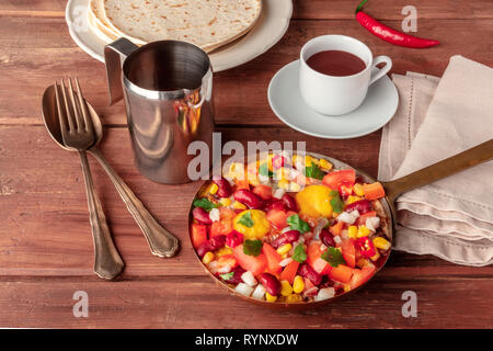 Colazione messicana. Huevos rancheros, le uova fritte con il Pico de Gallo insalata, cioccolata calda e tortillas al buio su un rustico sfondo di legno Foto Stock