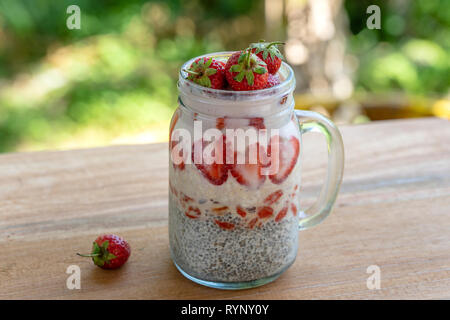 Latte di mandorle budino di Chia con rosso fresco Fragole, goji bacche e fiocchi di avena in un vasetto di vetro mug. Vegan materie prima colazione. Semi di Chia e fresco tagliato fr Foto Stock