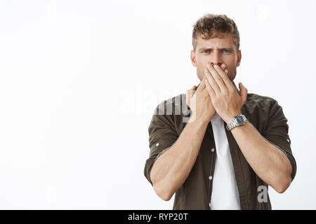 Vita-up shot dei delusi e sconvolti bionda uomo nel guardare e abiti casual che copre la bocca con palme e accigliata, smorfie insoddisfatto e Foto Stock