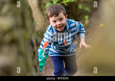 Un piccolo ragazzo in abiti luminosi si arrampica attraverso una foresta mentre sorridente Foto Stock