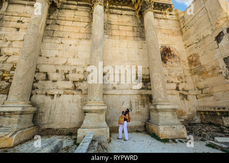 Una giovane donna mira la sua fotocamera presso l'antica Adriana parete libreria in età romana Agorà di Atene in Grecia. Foto Stock