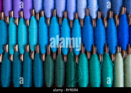 Immagine di tre righe di colorati rocca thread, cucitura o cucitura di blu, verde scuro, beige e colori viola Foto Stock