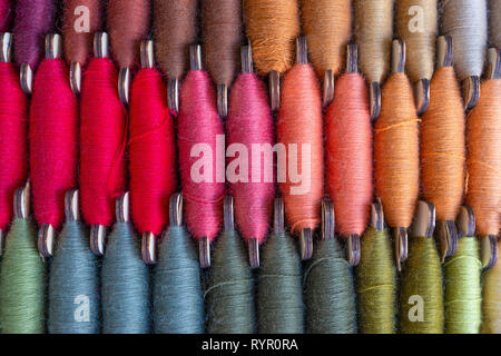 Immagine di tre righe di colorati rocca thread, cucitura o cucitura del rosso, arancio, marrone e di altri colori Foto Stock