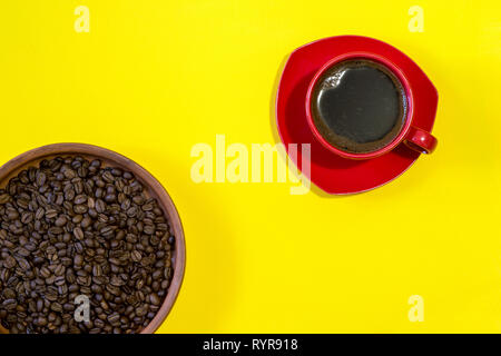 Red tazza di caffè appena fatto con fagioli arrosto in una ceramica pentola di creta su sfondo giallo. Vista superiore, piatto laici. Foto Stock