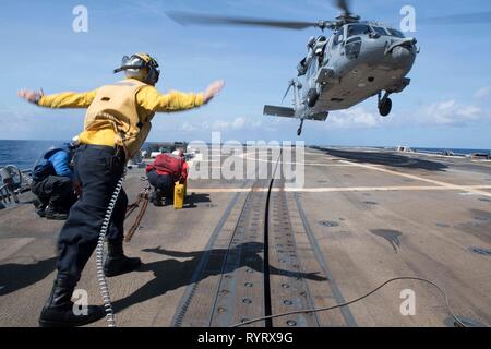 Stati Uniti Marina di Boatswain Mate 3° di classe Brandon Ross, da Honeapath, Carolina del Sud, segnali i piloti di un MH-60S elicottero, assegnato al mare in elicottero Combat Squadron 14, di atterrare sul ponte di volo dell'guidato-missile destroyer USS Spruance (DDG 111) durante le operazioni di volo sul Mare della Cina del Sud, Feb 24, 2019. Il Spruance è distribuito negli Stati Uniti 7 flotta area di operazioni a sostegno della sicurezza e della stabilità nella regione Indo-Pacifico. (U.S. Foto di Marina di Massa lo specialista di comunicazione 1a classe Ryan D. McLearnon) Foto Stock