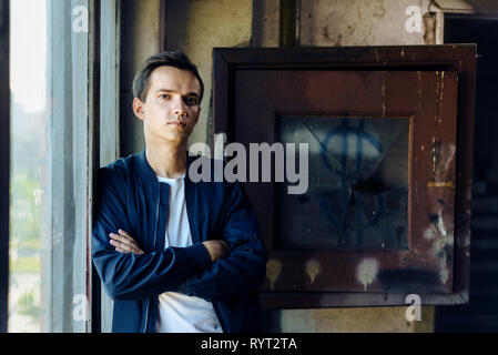 Ritratto di giovane uomo in camicia sorge vicino alla finestra e rotto con vetro Foto Stock