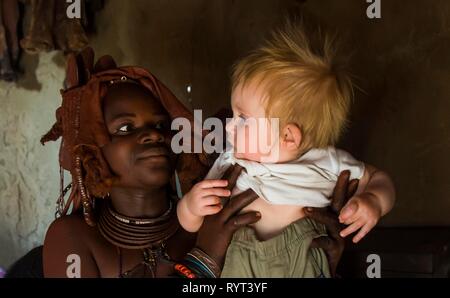 Donna Himba tenendo un turista bianco baby, Kaokoland, Namibia Foto Stock