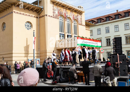 Sopron, Ungheria. Xv Mar, 2019. Un gruppo di ballerini folk tradizionale esegue Danze Ungheresi sul palco davanti al teatro in piazza Petőfi, Sopron, Ungheria. Il molino fisso sul balcone del teatro dice "il nostro paese è la più importante', una citazione di Ferenc Kölcsey, poeta ungherese. Credito: Wahavi/Alamy Live News Foto Stock