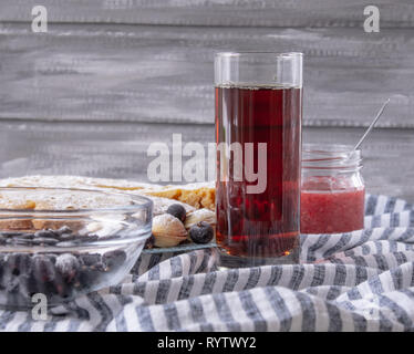 Succo rosso in un bicchiere accanto a una ciotola di cookie e di un vasetto di marmellata, close-up. Foto Stock