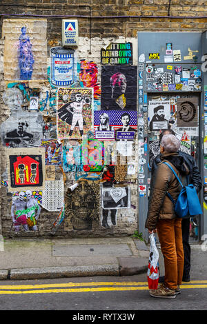 Un coiuple fermatevi e guardate il poster assortiti e illustrazione con graffiti su un muro in East End di Londra, Regno Unito. Foto Stock