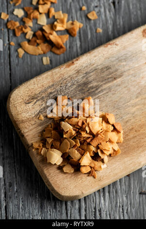 Angolo alto in prospettiva di una pila di pezzi di cocco candita su un tagliere di legno, collocata sul grigio di una tavola in legno rustico Foto Stock