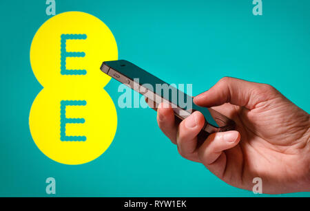 Un uomo con un telefono cellulare nella parte anteriore di un EE mobile segno di rete Foto Stock