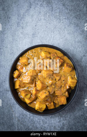 Malai paneer formaggio indiano curry in una grande ciotola nera con una vista superiore e con uno sfondo grigio. Spessore di paneer cremoso curry nel centro. Piatti vegetariani Foto Stock