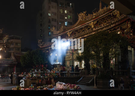 Tempio Lungshan, storico buddista e il Tempio Taoista, fumi di combustione degli incensi e fedeli si radunano attorno all altare, visto di notte, Taipei, Taiwan Foto Stock