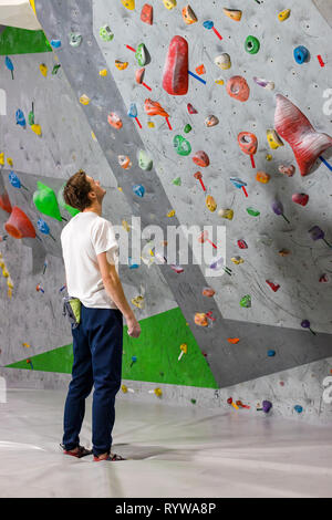 Rocciatore si alza e guarda la parete di arrampicata con ganci in boulder hall Foto Stock