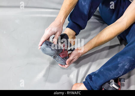 Rocciatore mette il roccioso di scarpe in una sala bouldering in una palestra di arrampicata Foto Stock