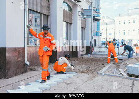 Mosca, Russia - Agosto 14, 2015: builderworkers prevista una nuova piastrella sul marciapiede. La ricostruzione di pavimentazione piastrelle nella capitale vicino a palace Chertkov Foto Stock