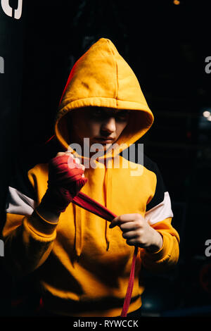 Donna boxer in felpa gialla tira bende rosse sulle mani. Foto Stock