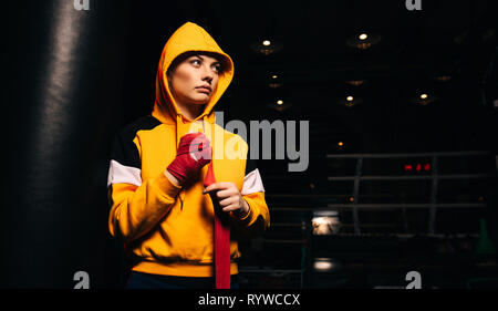 Sport ragazza boxer in felpa gialla tira bende rosse sulle mani. Foto Stock