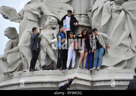 Gli studenti la scalata al Queen Victoria Memorial fuori Buckingham Palace a Londra durante la scuola globale sciopero per il cambiamento climatico. Foto Stock