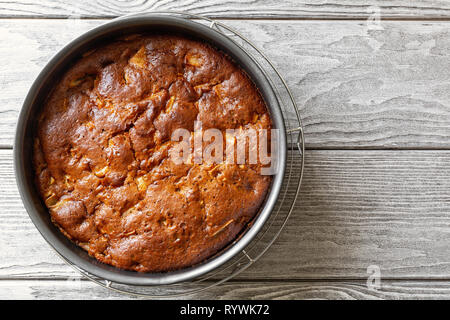 Appena sfornato odore deliziosa torta di mele charlotte si raffredda in forma culinaria su un tavolo di legno. Vegan la torta di mele senza uova senza burro, top Foto Stock