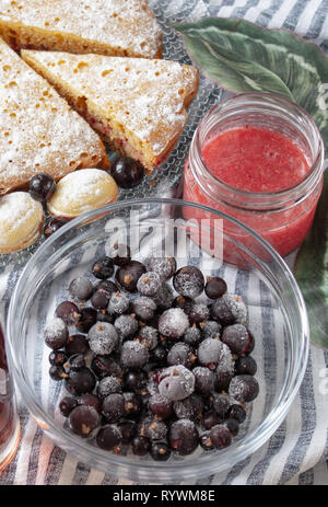 Bacche di ribes surgelati in una ciotola di vetro. Il ghiaccio sulle bacche. Bacche scure nel ghiaccio. Foto Stock