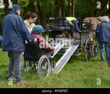 In sedia a rotelle rider essendo spinto verso l'alto una rampa su un carrello su una carrozza a giorno eseguire dall'equitazione per disabili Associazione, Wiltshire, Regno Unito. Foto Stock