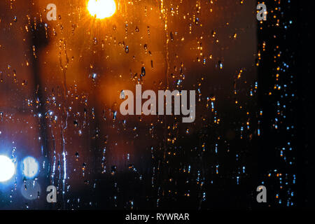 Gocce di pioggia su una lastra di vetro su sfondo evidenziato dalla torcia elettrica. Gocce di acqua su un vetro di un finestrino Foto Stock