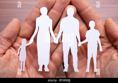 Famiglia di carta ritagliata con la protezione delle mani a tazza sulla scrivania in legno Foto Stock