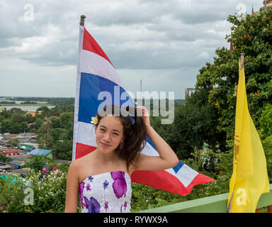 Sorridente teen in piedi di fronte a bandiera tailandese con città in background Foto Stock