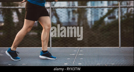 Giovane uomo sportivo gambe in esecuzione all'aperto lungo un ponte al mattino. Auto conquistando superare ostacoli e vincere. Uno stile di vita sano concetto. Allenamento jo Foto Stock