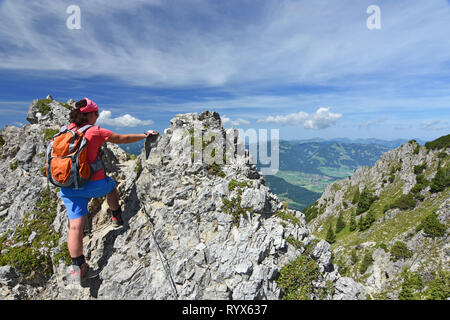 Escursionista femmina salendo a cresta esposta vicino a Oberstdorf in Algovia orientale delle Alpi, Baviera, Germania. Paesaggio alpino con montagne rocciose, foresta, cielo blu. Foto Stock