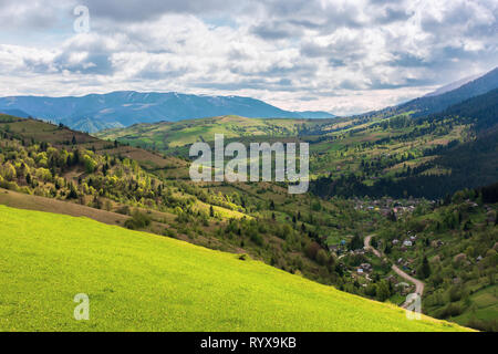 Campagna montuosa in primavera. villaggio nella valle, campi rurali sulle colline. distante montagna cresta con macchie di neve. tempo soleggiato con clo Foto Stock