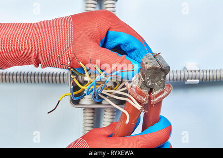 Repairman nei guanti di protezione è il taglio delle estremità dei fili con del tronchese strumento durante l'installazione di scatola di giunzione. Foto Stock