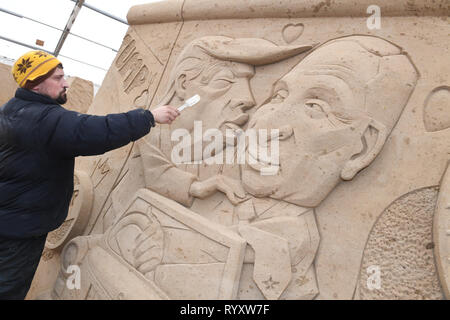 Binz, Germania. Xii Mar, 2019. Lo scultore Wlodek Bludnik dalla Polonia sta lavorando sulla scultura di sabbia "Muro di Berlino" con una versione moderna del graffito del fratello bacio sulla motivazione della scultura di sabbia Festival. Essa ci mostra il presidente Donald Trump e il Presidente russo Vladimir Putin. Artisti provenienti da vari paesi europei stanno attualmente creando 45 cifre enormi per il decimo la scultura di sabbia Show nel Mar Baltico località balneare di Binz. La scultura di sabbia mostra apre il 16.03.2018. Credito: Stefan Sauer/dpa-Zentralbild/dpa/Alamy Live News Foto Stock