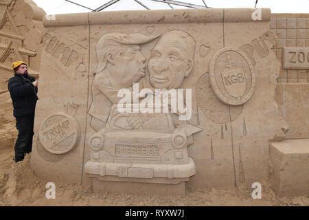 Binz, Germania. Xii Mar, 2019. Lo scultore Wlodek Bludnik dalla Polonia sta lavorando sulla scultura di sabbia "Muro di Berlino" con una versione moderna del graffito del fratello bacio sulla motivazione della scultura di sabbia Festival. Essa ci mostra il presidente Donald Trump e il Presidente russo Vladimir Putin. Artisti provenienti da vari paesi europei stanno attualmente creando 45 cifre enormi per il decimo la scultura di sabbia Show nel Mar Baltico località balneare di Binz. La scultura di sabbia mostra apre il 16.03.2018. Credito: Stefan Sauer/dpa-Zentralbild/dpa/Alamy Live News Foto Stock